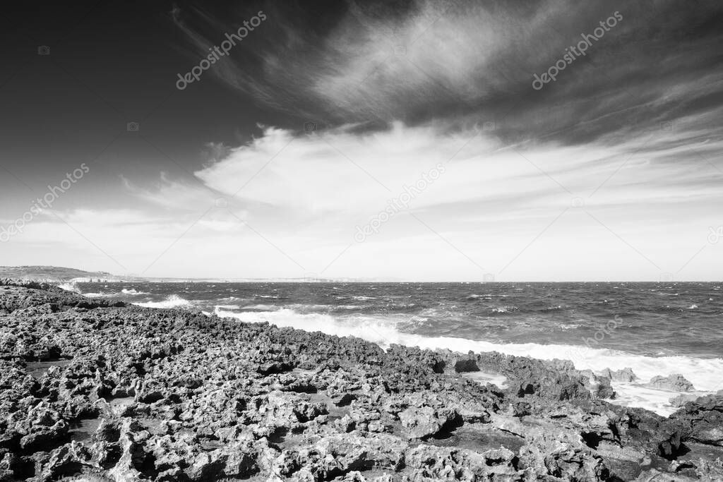 rocky beach in malta looking out to the sea with a cloudy sky