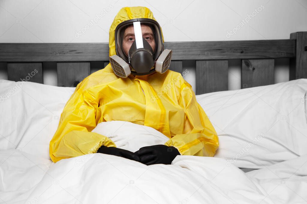 person self isolating in bed wearing a hazmat suit and mask