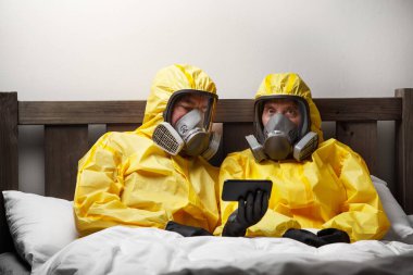 İki kişi yatakta yalnızlık çekiyor. Çok dikkatli davranıyorlar ve tehlikeli madde kıyafeti giyiyorlar.