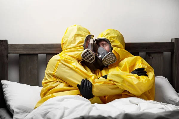 İki kişi yatakta yalnızlık çekiyor. Çok dikkatli davranıyorlar ve tehlikeli madde kıyafeti giyiyorlar.