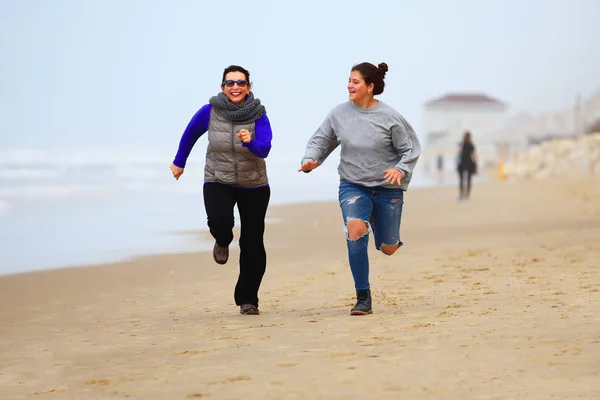 Mother and daughter running on sand during winter time — Stock Photo, Image