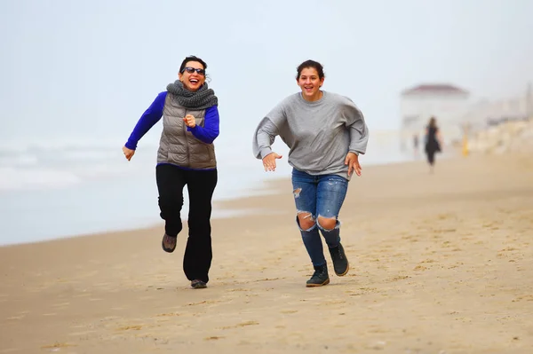 Mother and daughter running on sand during winter time — Stock Photo, Image