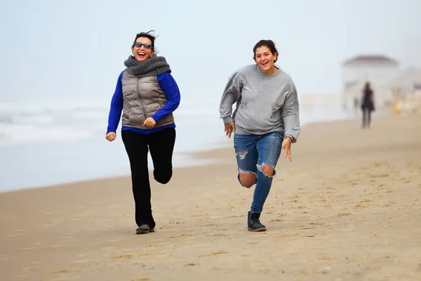 Mother and daughter running on sand during winter time — Stock Photo, Image