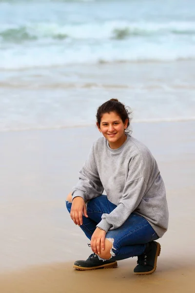 Junges Mädchen sitzt im Winter am Strand vor dem Meer — Stockfoto