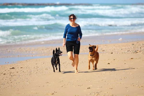 Mulher madura brincando com seus cães na praia — Fotografia de Stock