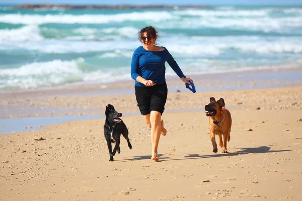 Mulher madura brincando com seus cães na praia — Fotografia de Stock