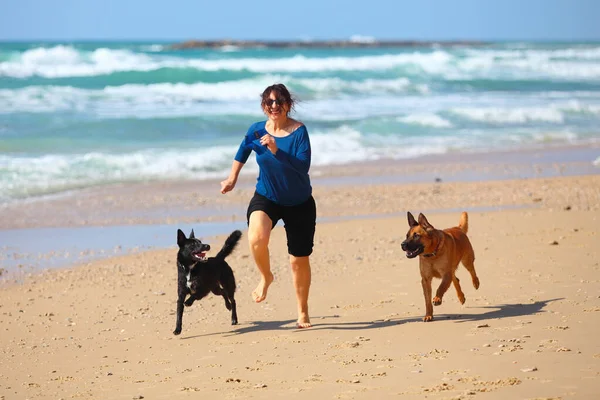 Mulher madura brincando com seus cães na praia — Fotografia de Stock