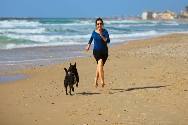 Gammal kvinna leker med sin hund på stranden. — Stockfoto