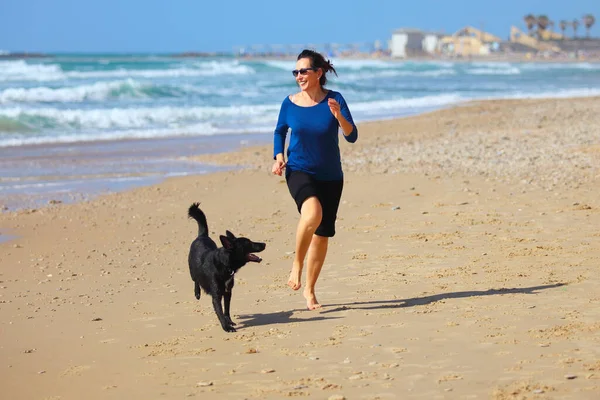 成熟女人在海滩上和她的狗玩耍 — 图库照片