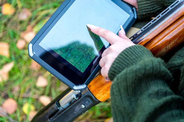 Women's hands with a nice manicure point to point on the area map, view card on a secure tablet computer on a background of a hunting rifle — Stock Photo, Image