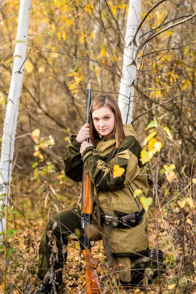 Portrait of a beautiful young girl hunter in camouflage clothes in the deciduous forest in nature with a gun — Stock Photo, Image