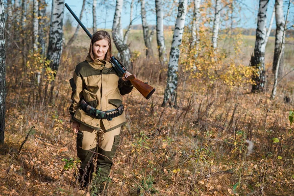 Retrato de una hermosa joven cazadora en ropa de camuflaje en el bosque caducifolio en la naturaleza con una pistola — Foto de Stock