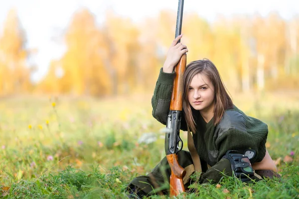 Portrait of a beautiful young girl hunter in camouflage clothes in the deciduous forest in nature with a gun — Stock Photo, Image