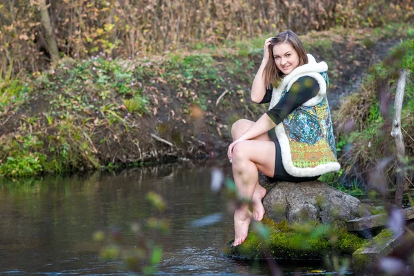 Portret van een mooi jong meisje in modieuze kleding op een achtergrond van de natuur — Stockfoto