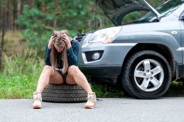 美丽的年轻女子修理一辆破的车在一个领域，换轮子。我休息，累了，坐下来，抓着她的头 — 图库照片