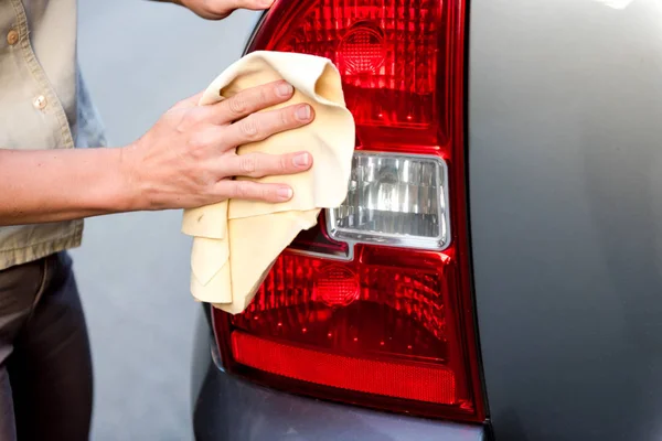 Handen van een mooi jong meisje wassen van een auto met een microfiber doek veegt koplampen en innerlijke panel van de auto, auto handwas — Stockfoto