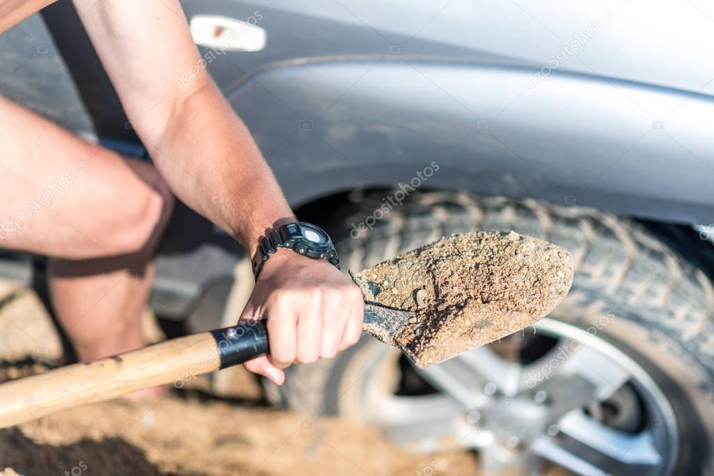 a man digs a car stuck in the sand, throwing sand shovel out fro