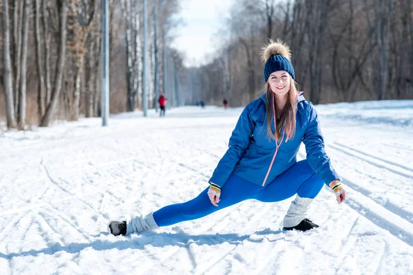 Mooi jong meisje zich uitstrekt op een sportveld in de winter weer — Stockfoto