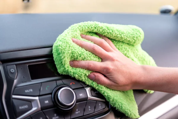 A female hand with a microfibre cloth cleans the panel of a modern car and the radio tape recorder from dust, the concept of professional washing or car wash