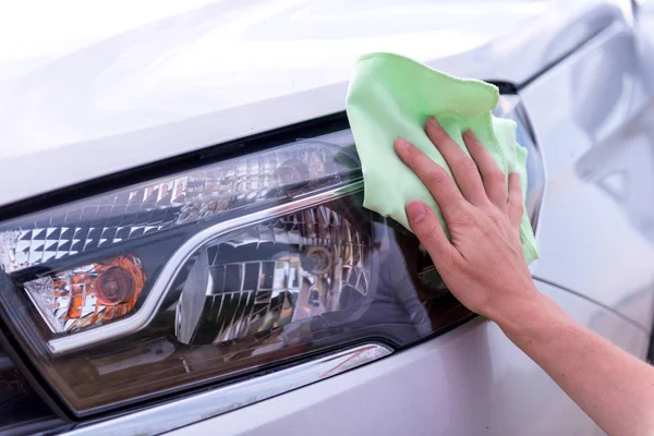 A female hand with a microfibre cloth cleans the headlights, the — Stock Photo, Image