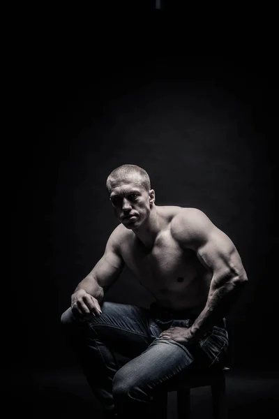 Portréja egy ülő férfi testépítő, egy fekete háttér ISO — Stock Fotó