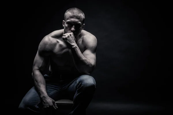 portrait of a seated male bodybuilder, on a black background iso