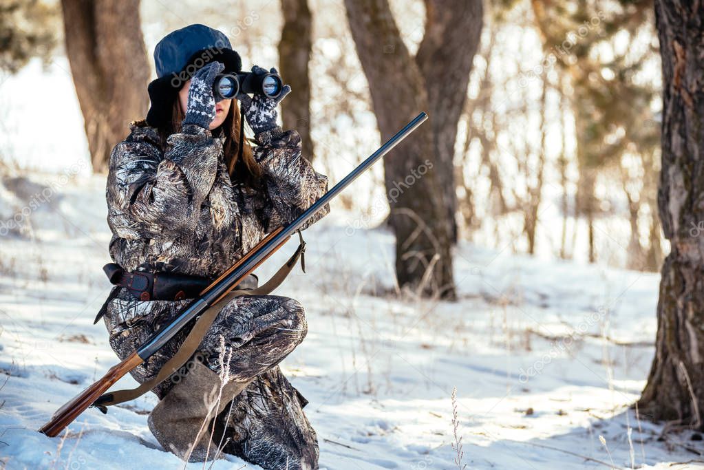 female hunter in camouflage clothes ready to hunt, holding gun a