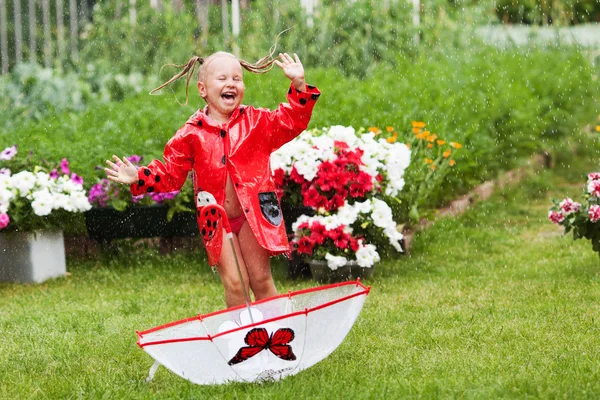 Fröhlicher Spaß hübsches kleines Mädchen in rotem Regenmantel mit Regenschirm spazieren im Park Sommer — Stockfoto