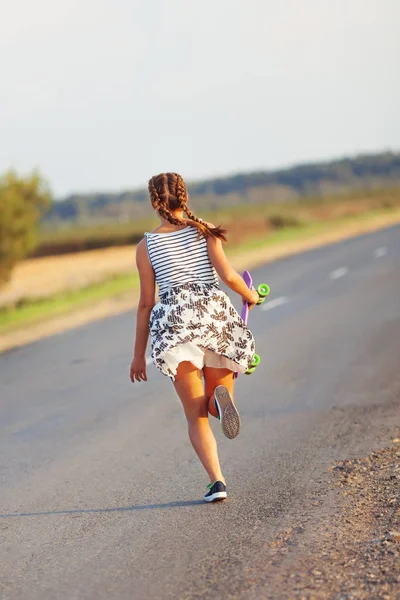 Roztomilá dívka jede skateboard na silnici — Stock fotografie
