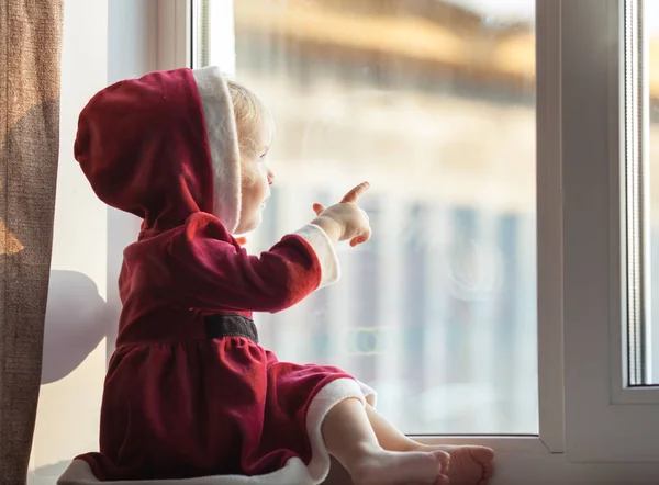 Маленькая симпатичная девочка в костюме Санты смотрит в окно — стоковое фото