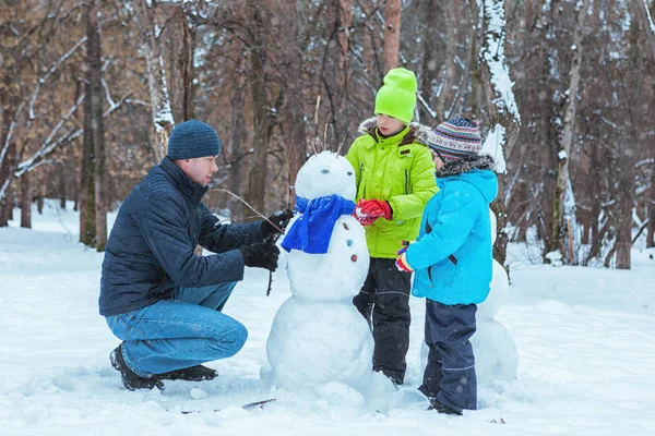 Pai feliz e dois filhos moldam boneco de neve no parque de inverno — Fotografia de Stock