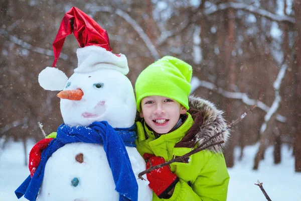Menyenangkan, anak bahagia bermain dengan manusia salju di taman musim dingin — Stok Foto