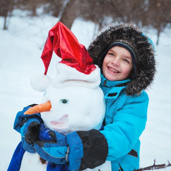 Зимнее веселье, счастливый ребенок играет со снеговиком — стоковое фото