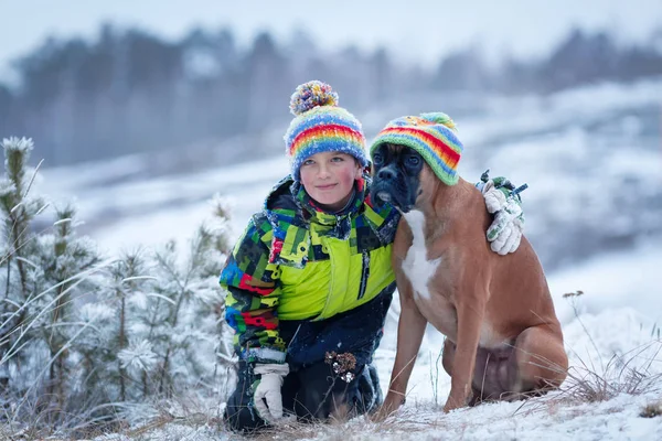 Portret van gelukkige jongen met de hond in de hoed op winter bos achtergrond — Stockfoto