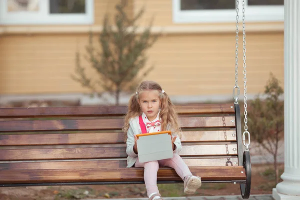 Serieus meisje is bezig op een tablet, ze zit op een houten bank op de binnenplaats van het huis — Stockfoto