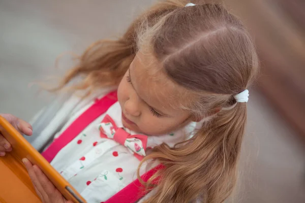 Serieus meisje is bezig op een tablet, ze zit op een houten bank op de binnenplaats van het huis — Stockfoto