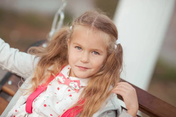 Happy girl is sitting on a wooden swing in the courtyard of the house. Outdoor, summer. — Stock Photo, Image