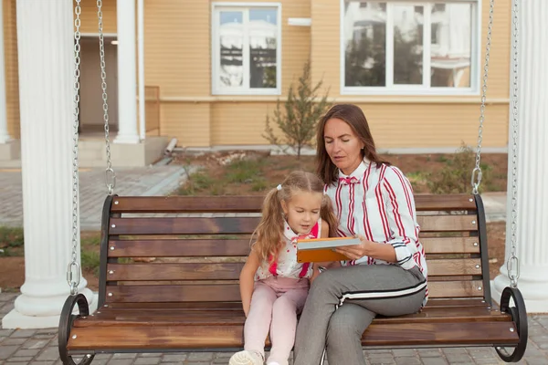 Emotioneel portret van een positief en vrolijk meisje met krullend haar, kijkend naar haar moeder. Gelukkige jeugd. Mam en dochter studeren op de tablet. — Stockfoto