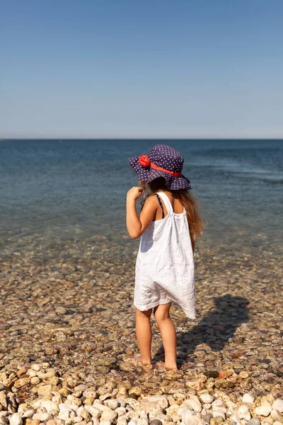 Porträt des niedlichen fröhlichen, glücklichen Mädchens mit Hut, im Freien. Mädchen steht am Ufer des Meeres. — Stockfoto