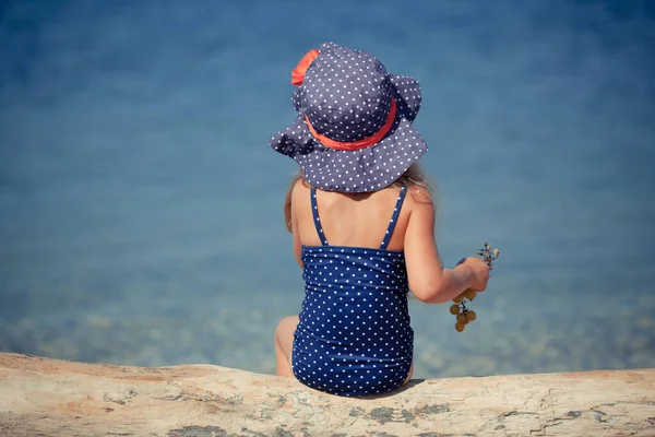 Porträt eines niedlichen, fröhlichen Mädchens mit Hut und Sonnenbrille, im Freien. Mädchen sitzt am Strand. — Stockfoto