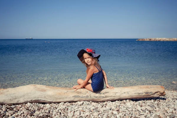 Porträt eines niedlichen, fröhlichen Mädchens mit Hut und Sonnenbrille, im Freien. Mädchen sitzt am Strand. — Stockfoto