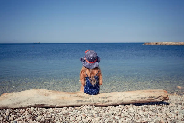 Porträtt av söt glad, glad flicka bär hatt och solglasögon, utomhus. Flicka som sitter på stranden. — Stockfoto