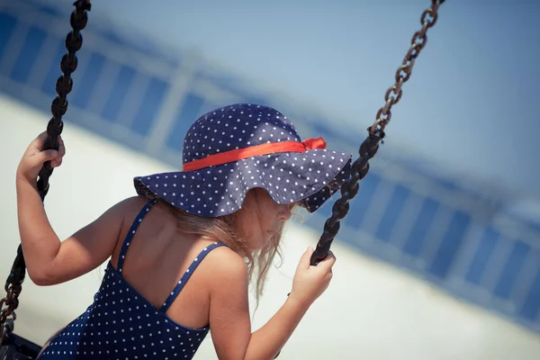 Chica en traje de baño y sombrero balanceándose en un columpio contra un cielo azul — Foto de Stock