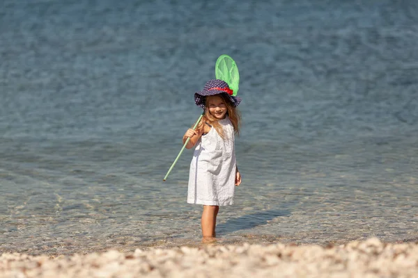 Porträt des niedlichen fröhlichen, glücklichen Mädchens mit Hut, im Freien. Mädchen steht am Ufer des Meeres. — Stockfoto