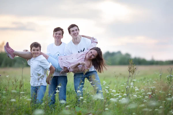 Ritratto di una grande famiglia felice su uno sfondo di natura estiva, una passeggiata nel campo, Tre figli tengono una mamma felice tra le braccia — Foto Stock