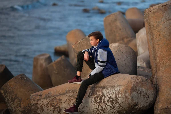 一个英俊而严肃的野蛮人的画像。 一个少年坐在海边的防波堤上. — 图库照片