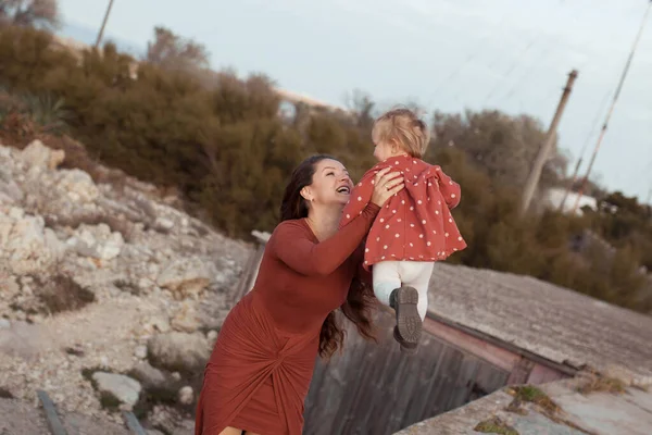 Ein kleines Mädchen und eine Mutter gehen am Meer spazieren, sie spielen und umarmen sich — Stockfoto