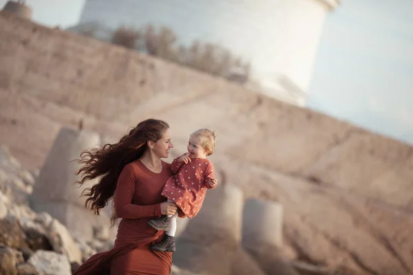 Ein kleines Mädchen und eine Mutter gehen am Meer spazieren, sie spielen und umarmen sich — Stockfoto