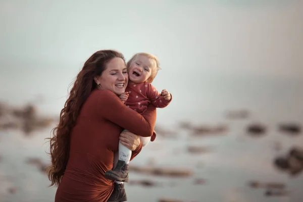 Een klein meisje en mama lopen vlak bij de zee, ze spelen en knuffelen — Stockfoto