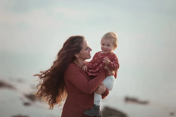 Ein kleines Mädchen und eine Mutter gehen am Meer spazieren, sie spielen und umarmen sich — Stockfoto